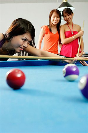 simsearch:656-01770739,k - Woman holding pool cue, aiming, women watching in the background Fotografie stock - Premium Royalty-Free, Codice: 656-01770740