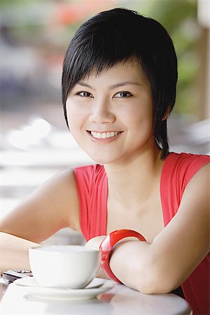 Woman smiling at camera, cup and saucer next to her Stock Photo - Premium Royalty-Free, Code: 656-01771596