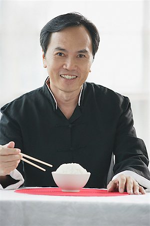 simsearch:656-01771940,k - Man with bowl of rice and chopsticks, smiling at camera Fotografie stock - Premium Royalty-Free, Codice: 656-01771974