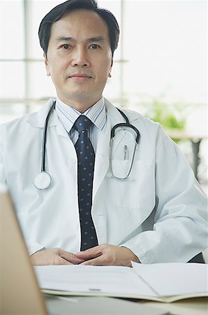 simsearch:656-01772656,k - Doctor sitting at desk, looking at camera, serious expression Stock Photo - Premium Royalty-Free, Code: 656-01771971