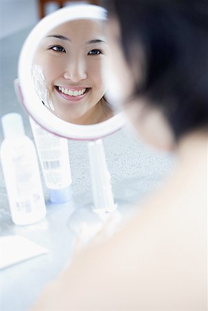 dermatologia - Young woman looking in mirror, over the shoulder view Fotografie stock - Premium Royalty-Free, Codice: 656-01772034