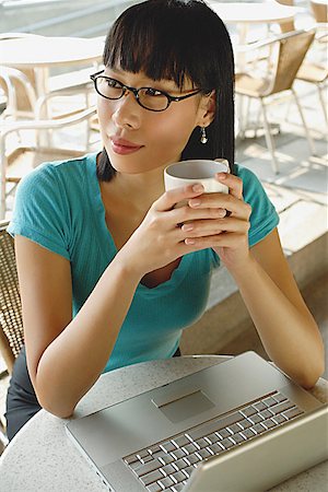 simsearch:656-01766118,k - Young woman in cafe, holding cup, laptop on table next to her, looking away Foto de stock - Royalty Free Premium, Número: 656-01772112