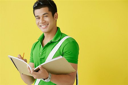 Young man writing in notebook, looking at camera Stock Photo - Premium Royalty-Free, Code: 656-01772280