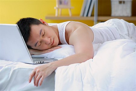 person being lazy on computer - Man lying on bed, sleeping, laptop next to him Stock Photo - Premium Royalty-Free, Code: 656-01772486