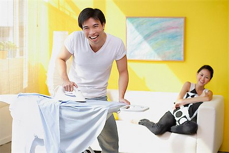 Couple at home, man ironing, woman sitting on sofa behind him Stock Photo - Premium Royalty-Free, Code: 656-01772544