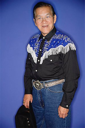 Senior man dressed in cowboy attire, standing against blue background, portrait Stock Photo - Premium Royalty-Free, Code: 656-01772596