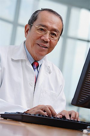simsearch:656-01772656,k - Doctor in office, using desktop computer, looking at camera Stock Photo - Premium Royalty-Free, Code: 656-01772662