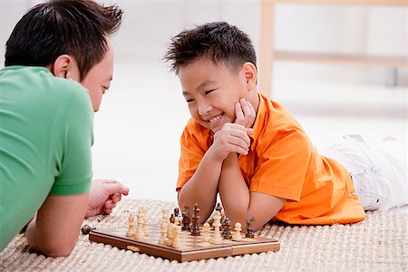 simsearch:656-01768260,k - Father and son lying on floor, playing chess, smiling Fotografie stock - Premium Royalty-Free, Codice: 656-01773032
