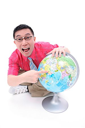 Man sitting on floor, pointing to globe, looking at camera Stock Photo - Premium Royalty-Free, Code: 656-01773096