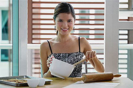 simsearch:656-01771940,k - Young woman in kitchen holding mixing bowl, smiling at camera Fotografie stock - Premium Royalty-Free, Codice: 656-01773420