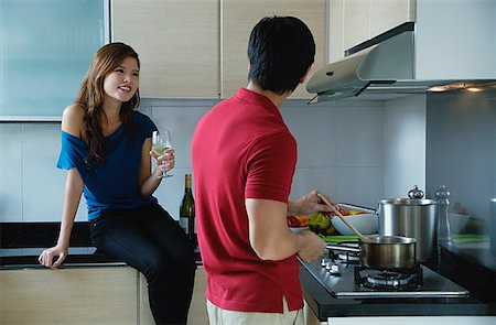 Man cooking in kitchen, looking at woman sitting on kitchen counter Foto de stock - Sin royalties Premium, Código: 656-01773467