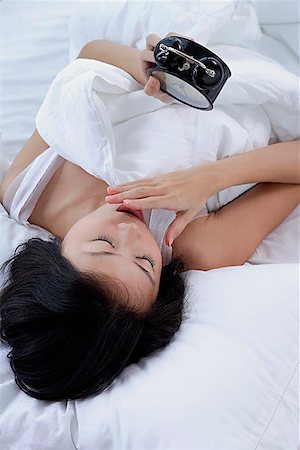 simsearch:656-01773560,k - Young woman on bed, looking at alarm clock, hand on mouth Stock Photo - Premium Royalty-Free, Code: 656-01773556