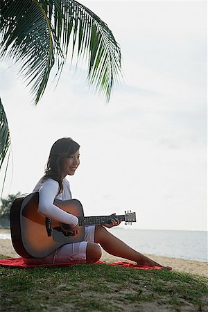 Young woman sitting on beach playing a guitar Stock Photo - Premium Royalty-Free, Code: 656-01773595