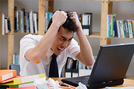 furious - Young man in library, pulling his hair, looking at laptop Stock Photo - Premium Royalty-Free, Code: 656-01773820