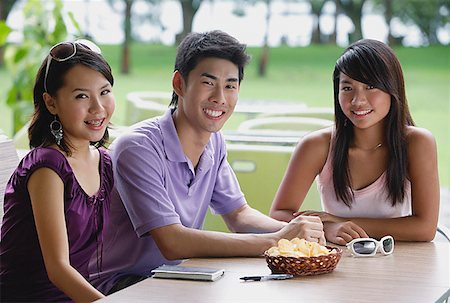 simsearch:656-01771940,k - Young adults sitting at outdoor cafe, smiling at camera Fotografie stock - Premium Royalty-Free, Codice: 656-01773957
