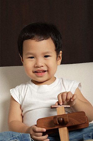 Baby boy holding wooden toy plane smiling at camera Stock Photo - Premium Royalty-Free, Code: 656-01828898