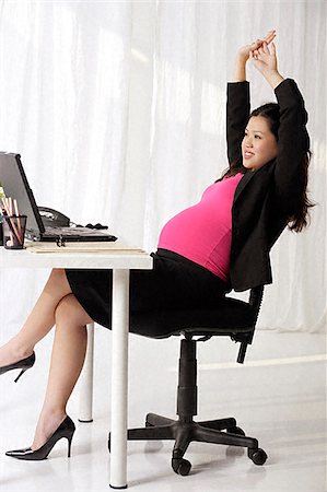 Profile of pregnant businesswoman at desk stretching Stock Photo - Premium Royalty-Free, Code: 656-02371805