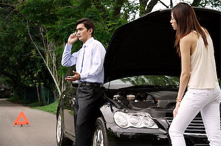 Woman looking under hood of car while man talks on phone Stock Photo - Premium Royalty-Free, Code: 656-02371879