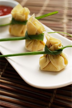 dimsum - 3 wanton dumplings placed in a row on a white plate with chili sauce on the side Stock Photo - Premium Royalty-Free, Code: 656-02702854