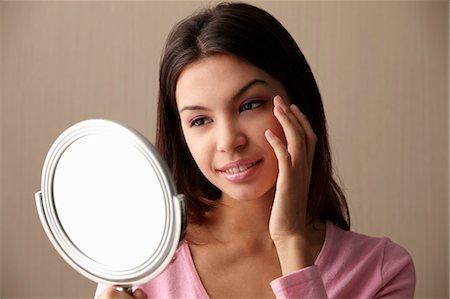 young woman looking at mirror touching her face Stock Photo - Premium Royalty-Free, Code: 656-03519543