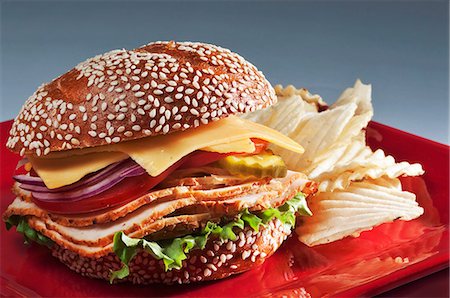 Sandwich à la dinde sur la graine de sésame rouler avec fromage américain, des tomates, des oignons et des cornichons ; Chips Photographie de stock - Premium Libres de Droits, Code: 659-06154913