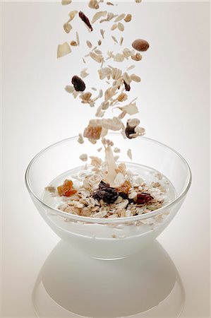 frühstücksflocken - Müsli-Zutaten (Getreide und Trockenobst) fallen in eine Schüssel mit Joghurt Stockbilder - Premium RF Lizenzfrei, Bildnummer: 659-06152081