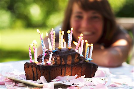 A birthday cake with burning candles and a young woman in the background Stock Photo - Premium Royalty-Free, Code: 659-06152256