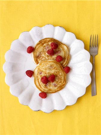 Two Pancakes with Fresh Raspberries on a White Plate; Yellow Background Stock Photo - Premium Royalty-Free, Code: 659-06152371