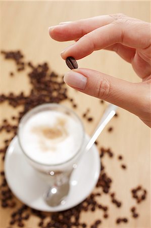 simsearch:659-08896141,k - Fingers holding a coffee bean over a glass of Latte Machhiato Fotografie stock - Premium Royalty-Free, Codice: 659-06153377