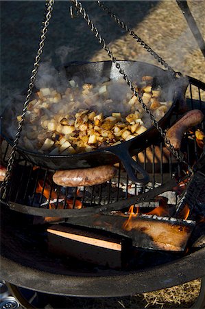 salsichão de porco - Potatoes and Brats Cooking Over and Open Fire Foto de stock - Royalty Free Premium, Número: 659-06153837