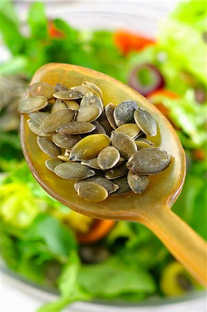 Graines de citrouille sur une cuillère au-dessus d'un bol de salade Photographie de stock - Premium Libres de Droits, Code: 659-06184910