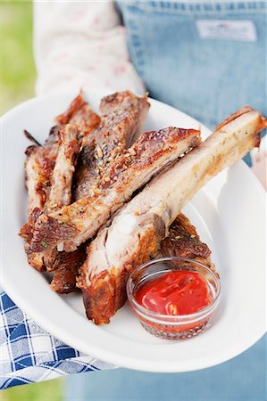 A person holding a plate of grilled spare ribs and barbecue sauce Stock Photo - Premium Royalty-Free, Code: 659-06186386