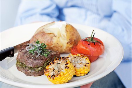 fillet beef recipes - A person holding a plate of grilled beef medallions, a jacket potato and grilled tomatoes and corn on the cob Stock Photo - Premium Royalty-Free, Code: 659-06186391