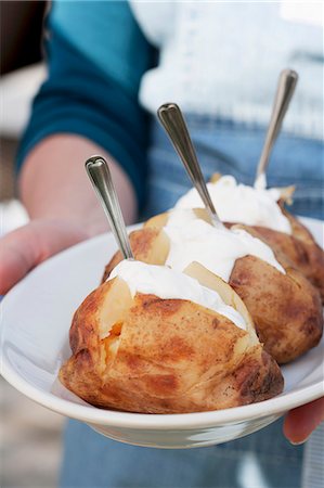 A person holding a plate of jacket potatoes with sour cream Stock Photo - Premium Royalty-Free, Code: 659-06186392