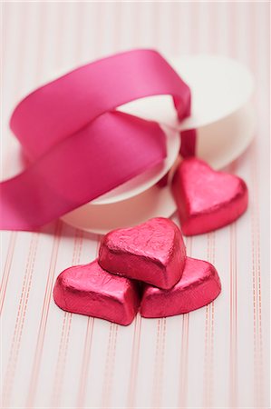 Heart-shaped chocolates wrapped in red foil and a red ribbon Stock Photo - Premium Royalty-Free, Code: 659-06187562