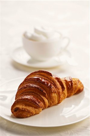 simsearch:659-06151130,k - Un croissant sur une plaque avec un cappuccino en arrière-plan Photographie de stock - Premium Libres de Droits, Code: 659-06307279