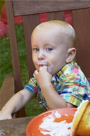 Little Boy Licking the Frosting Off His Fingers from a Cupcake; Sitting at an Outdoor Table Stock Photo - Premium Royalty-Free, Code: 659-06494673