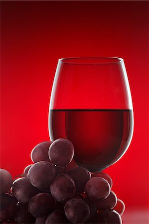 A glass of red wine and some red grapes against a red background Stock Photo - Premium Royalty-Free, Code: 659-06671364