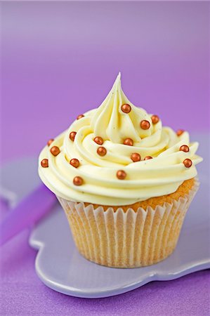 purple background - A cupcake with vanilla icing and gold sugar pearls in a paper case Stock Photo - Premium Royalty-Free, Code: 659-06671379