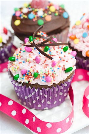 simsearch:659-06902206,k - Two cupcakes topped with pink buttercream icing, chocolate icing and sweets Foto de stock - Sin royalties Premium, Código: 659-06671384