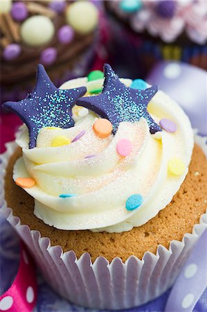 A vanilla cupcake with blue stars, glitter and sugar confetti Stock Photo - Premium Royalty-Free, Code: 659-06671385