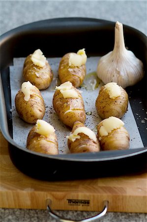 Raw Hasselback potatoes in a roasting tin, seasoned with salt, pepper and garlic butter Stock Photo - Premium Royalty-Free, Code: 659-06901985