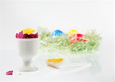 A boiled egg with the top cut off, in an eggcup, with an Easter nest of colourful eggs in the background Photographie de stock - Premium Libres de Droits, Code: 659-06902050