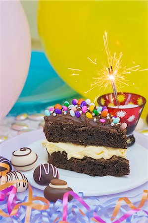 A piece of chocolate cake with colorful sprinkles and candy decorations for a party. Sparkler. Confections Foto de stock - Sin royalties Premium, Código: 659-06902169