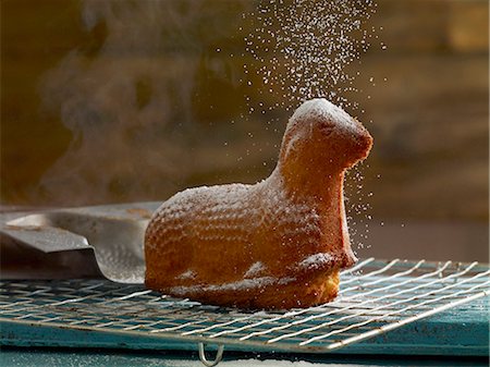 sugar sprinkling food photography - Easter lamb (cake) on cooling rack being sprinkled with powdered sugar Stock Photo - Premium Royalty-Free, Code: 659-06902322