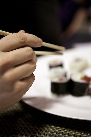 sushi plate - A hand reaching for a piece of sushi using chopsticks Stock Photo - Premium Royalty-Free, Code: 659-06902790