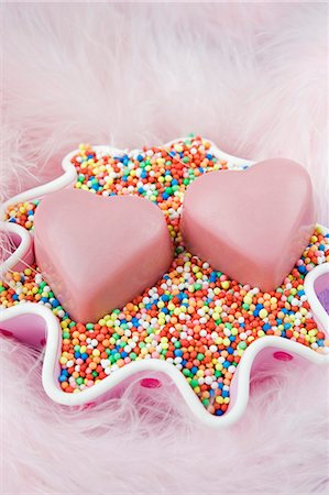 sugar pearl - two romantic pink love heart shaped chocolates for valentine s day, in a pink spotted cake cover laying on coloured hundreds and thousand sweets with pale pink feathers Stock Photo - Premium Royalty-Free, Code: 659-06903179