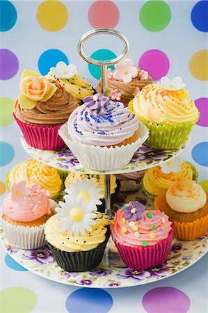 close up of purple, yellow and pink cup cakes decorated with icing flowers on a purple pansy flowered cake standon a coloured spotty background Foto de stock - Sin royalties Premium, Código: 659-06903189