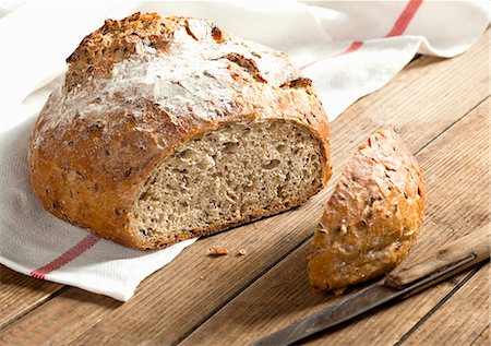 farmhouse bread - A fresh loaf of bread with the end sliced open, on a tea towel on a wooden surface Foto de stock - Sin royalties Premium, Código: 659-06903596