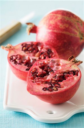 A whole and a halved pomegranate on a chopping board with a knife Foto de stock - Sin royalties Premium, Código: 659-07027915